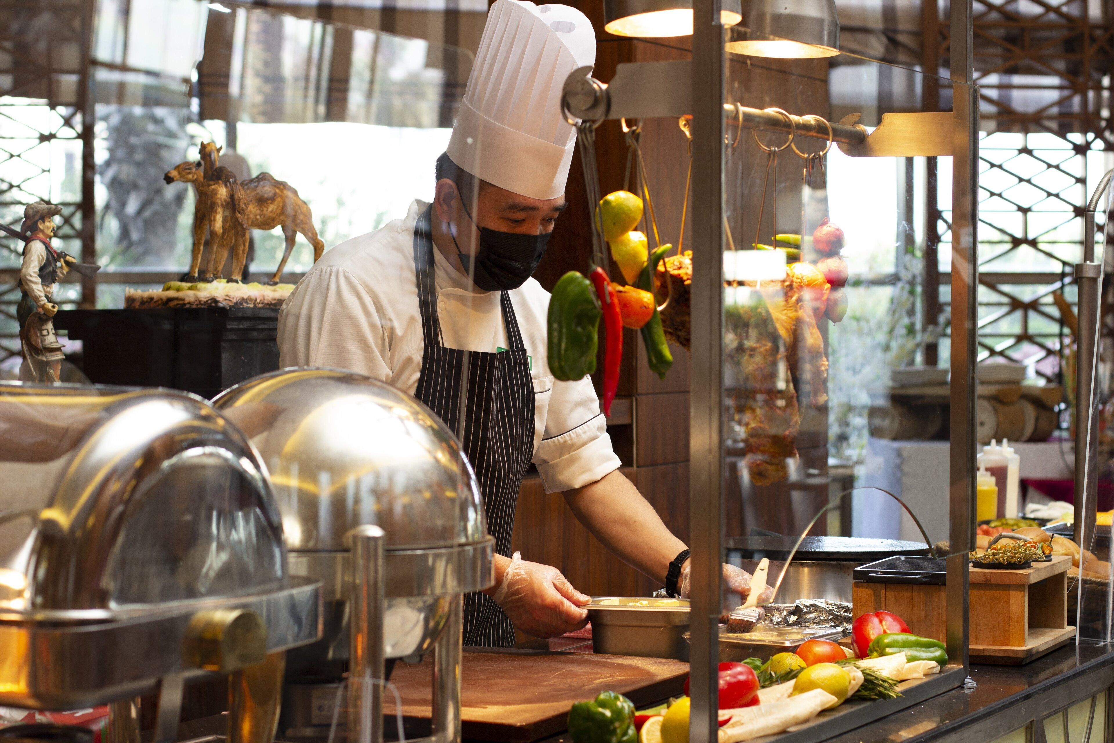 Un chef prépare des plats dans une cuisine où l’on peut voir divers légumes et ustensiles de cuisine.