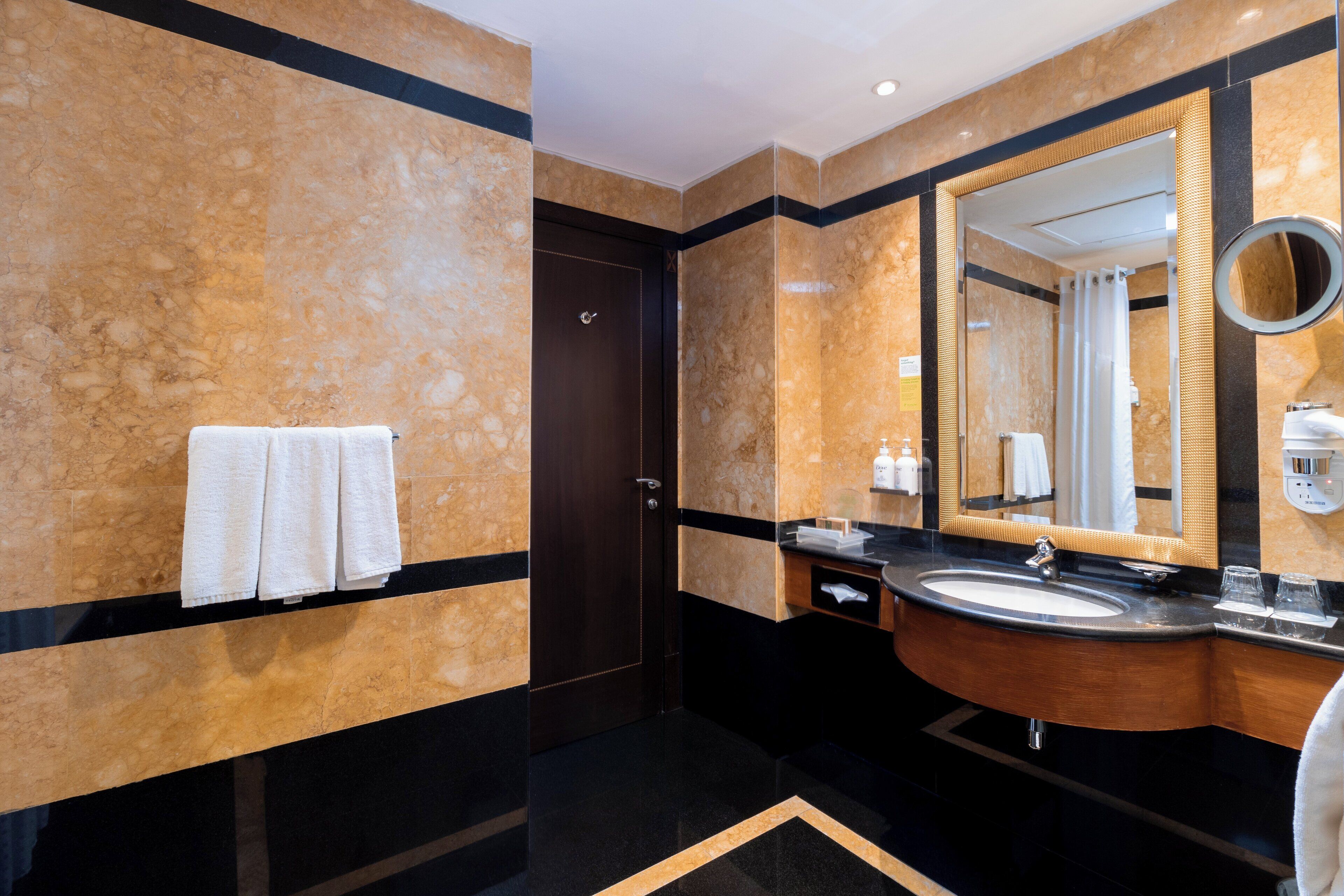 A modern bathroom with a marble wall, a wooden vanity, a large mirror, and a towel rack.