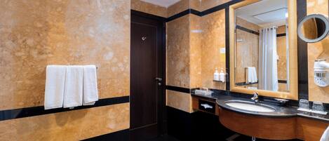 A modern bathroom with a marble wall, a wooden vanity, a large mirror, and a towel rack.
