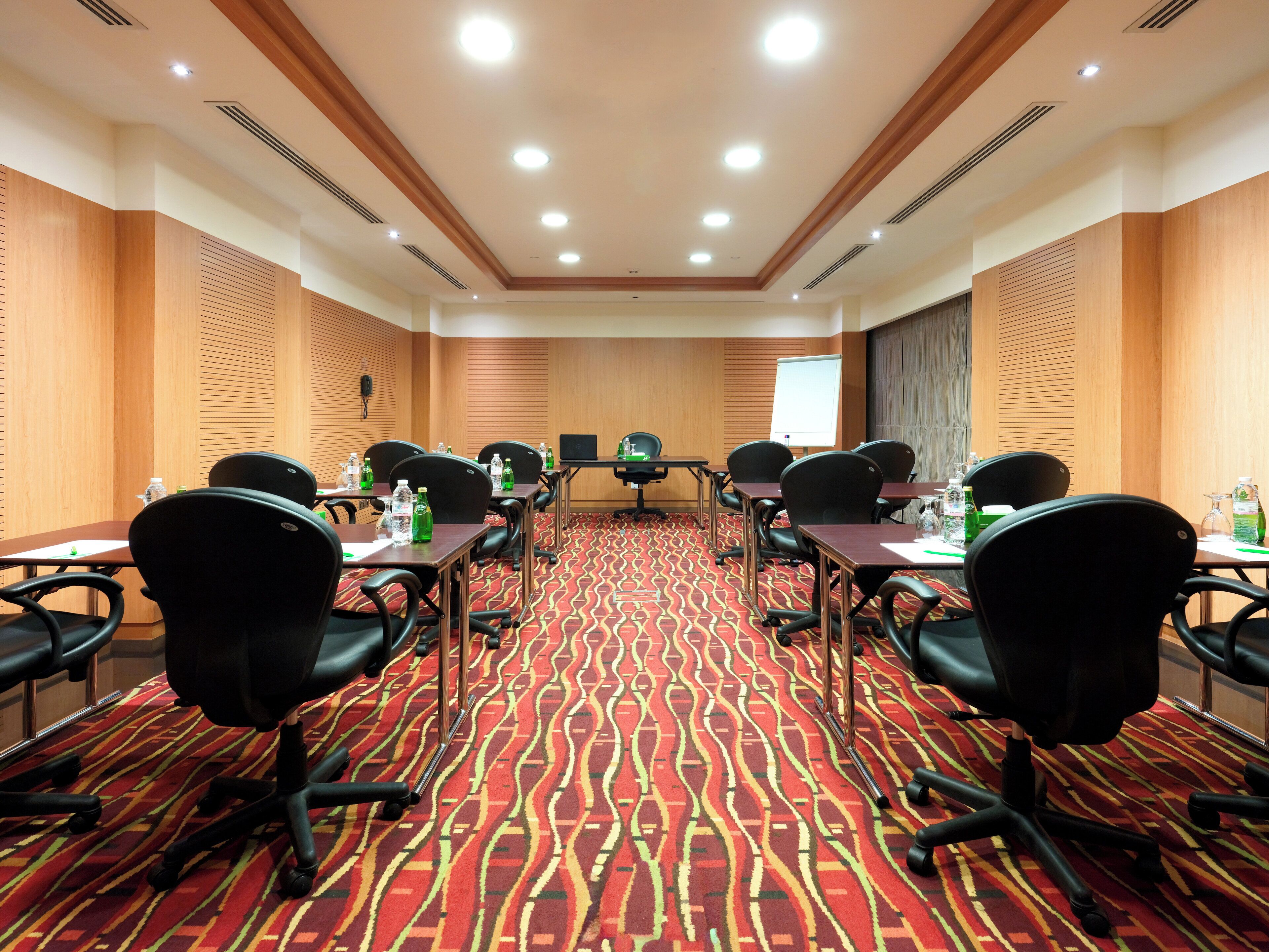 A conference room with a patterned carpet, wooden panel walls, and black office chairs.