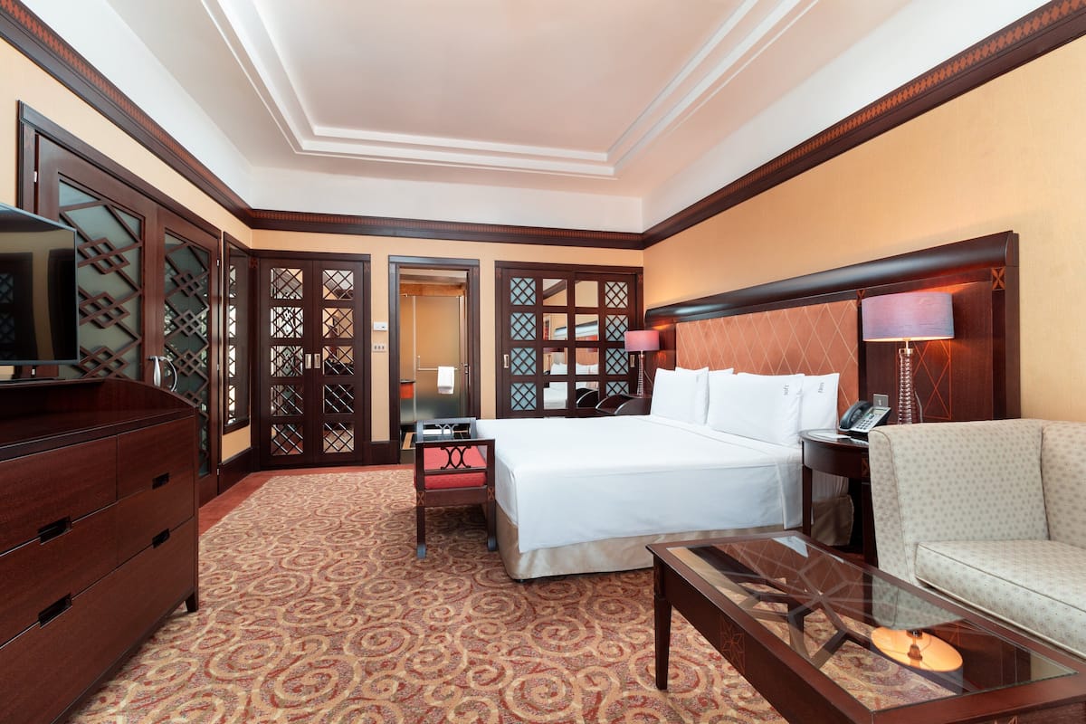 A hotel room with a bed, a desk, a chair, a dresser, and a TV.