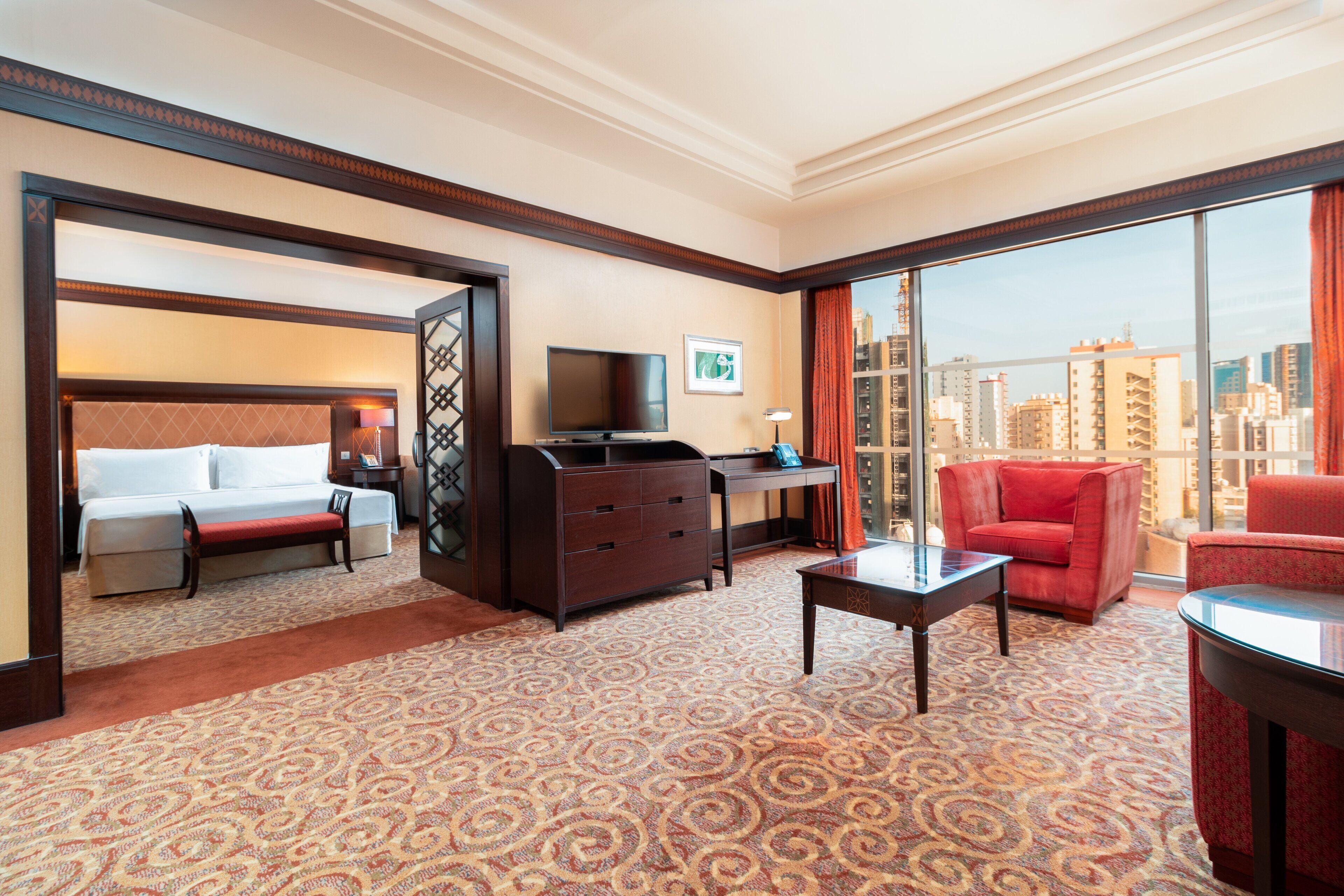 A hotel room with a bed, a desk, a TV, a red sofa, and a view of the city.