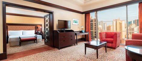 A hotel room with a bed, a desk, a TV, a red sofa, and a view of the city.