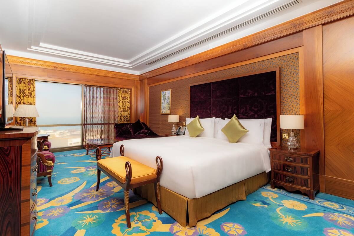 A hotel room with a large bed, a desk, a chair, and a view of the city.