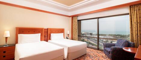 A hotel room with two beds, a large window with a city view, a patterned carpet, and a small table.