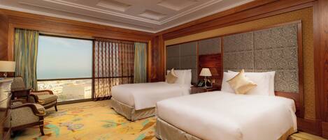 A hotel room with two beds, a large window with a view, a patterned carpet, and wooden paneling.
