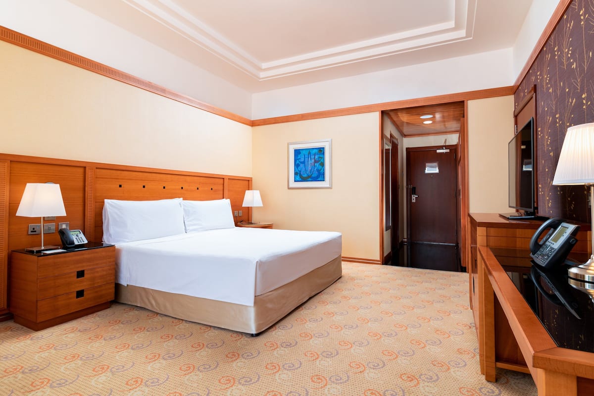 A hotel room with a large bed, two bedside tables with lamps, a desk with a telephone, and a door leading to the bathroom.