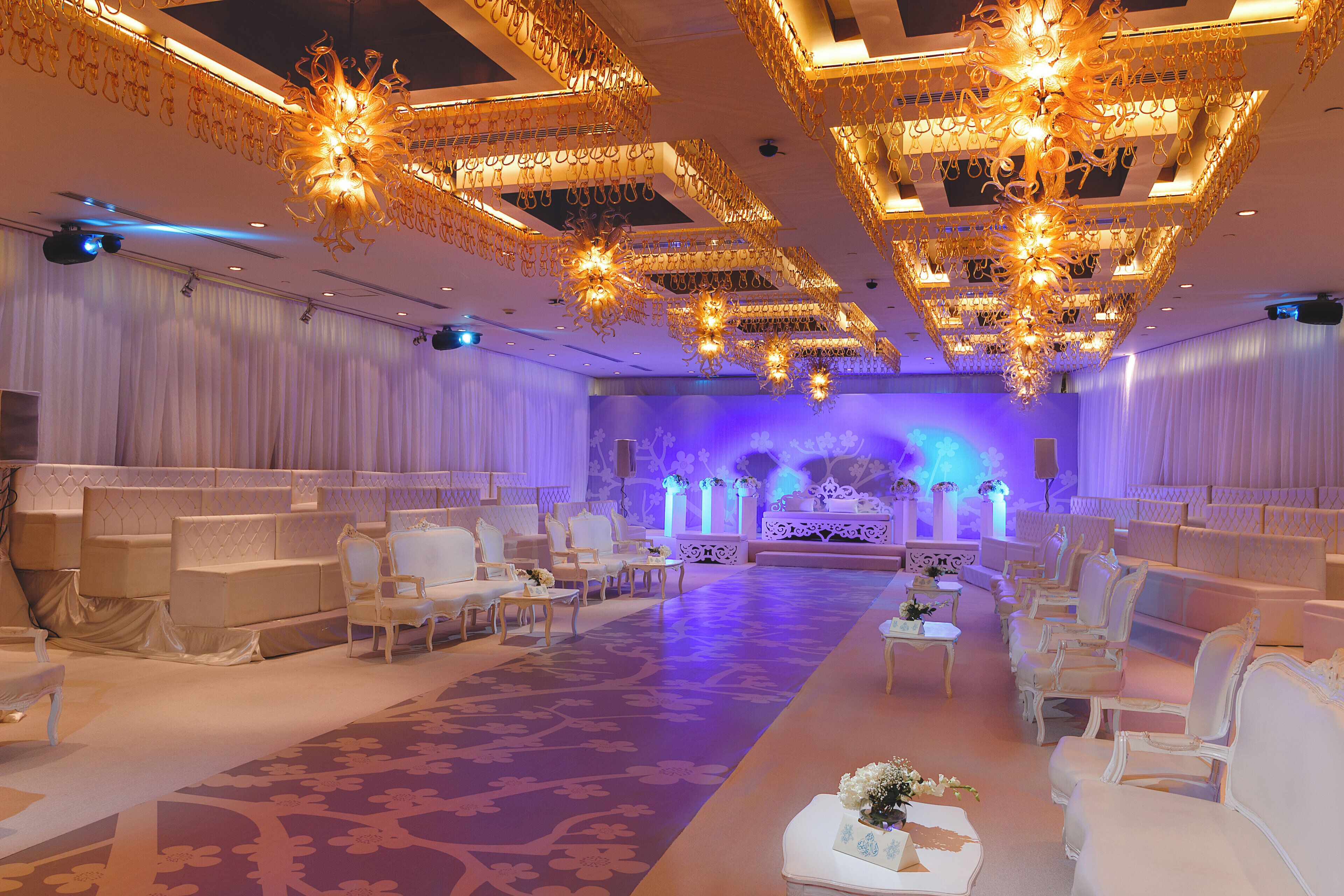 Un salón amplio con asientos escalonados, candelabros ornamentados y un escenario con decoraciones florales.