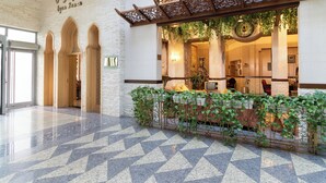 Un hall d’entrée doté d’un sol à motifs géométriques, d’un comptoir de réception agrémenté de plantes et d’un mur orné d’une rampe décorative en métal.