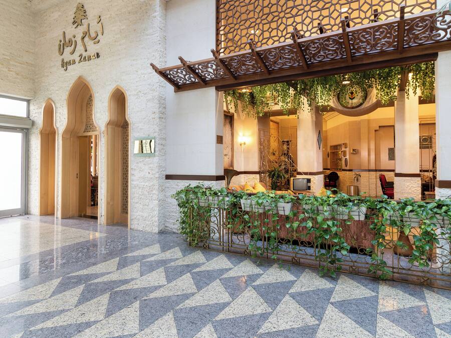 Un hall con piso de estampado geométrico, un mostrador de recepción con plantas y una pared con barandilla de metal decorativa.