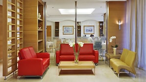 A modern lobby with red sofas, a wooden bookshelf, and a reception desk. - Athineon Hotel (Rhodes)