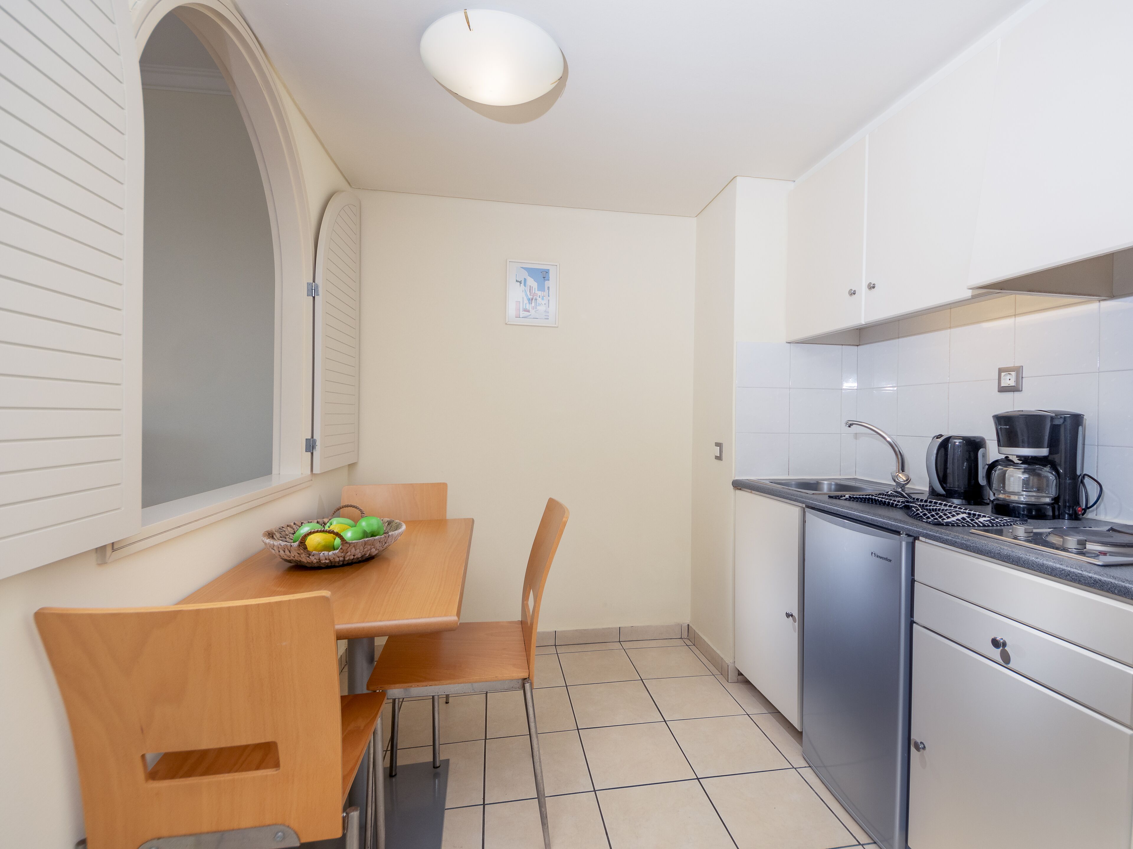 Cocina compacta con mesa, sillas, cafetera y lavabo.