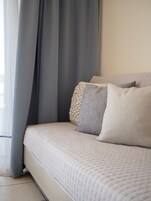 Una cama con cubrecolcha acolchado, almohadas grises y blancas, y una cortina gris.