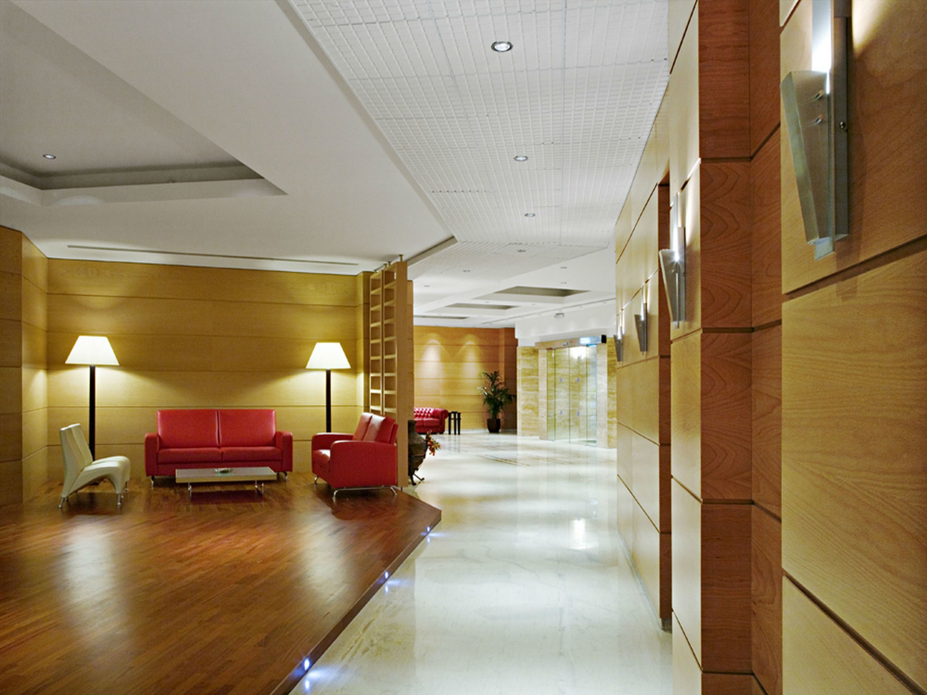 A hotel lobby with a wooden floor, red sofas, and a white ceiling with recessed lighting.