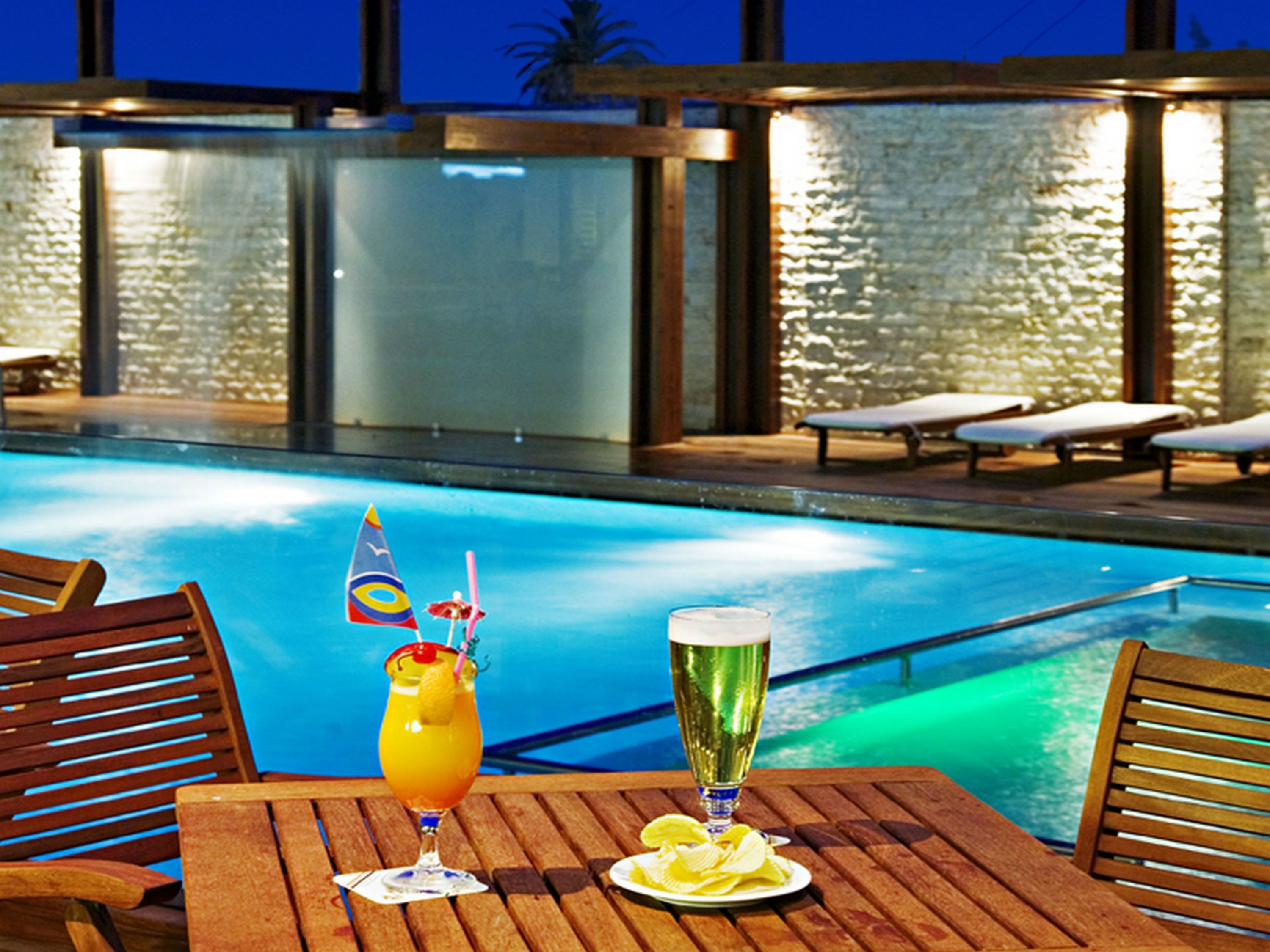 Un espace aménagé au bord de la piscine, avec une table, deux boissons et des chaises longues.