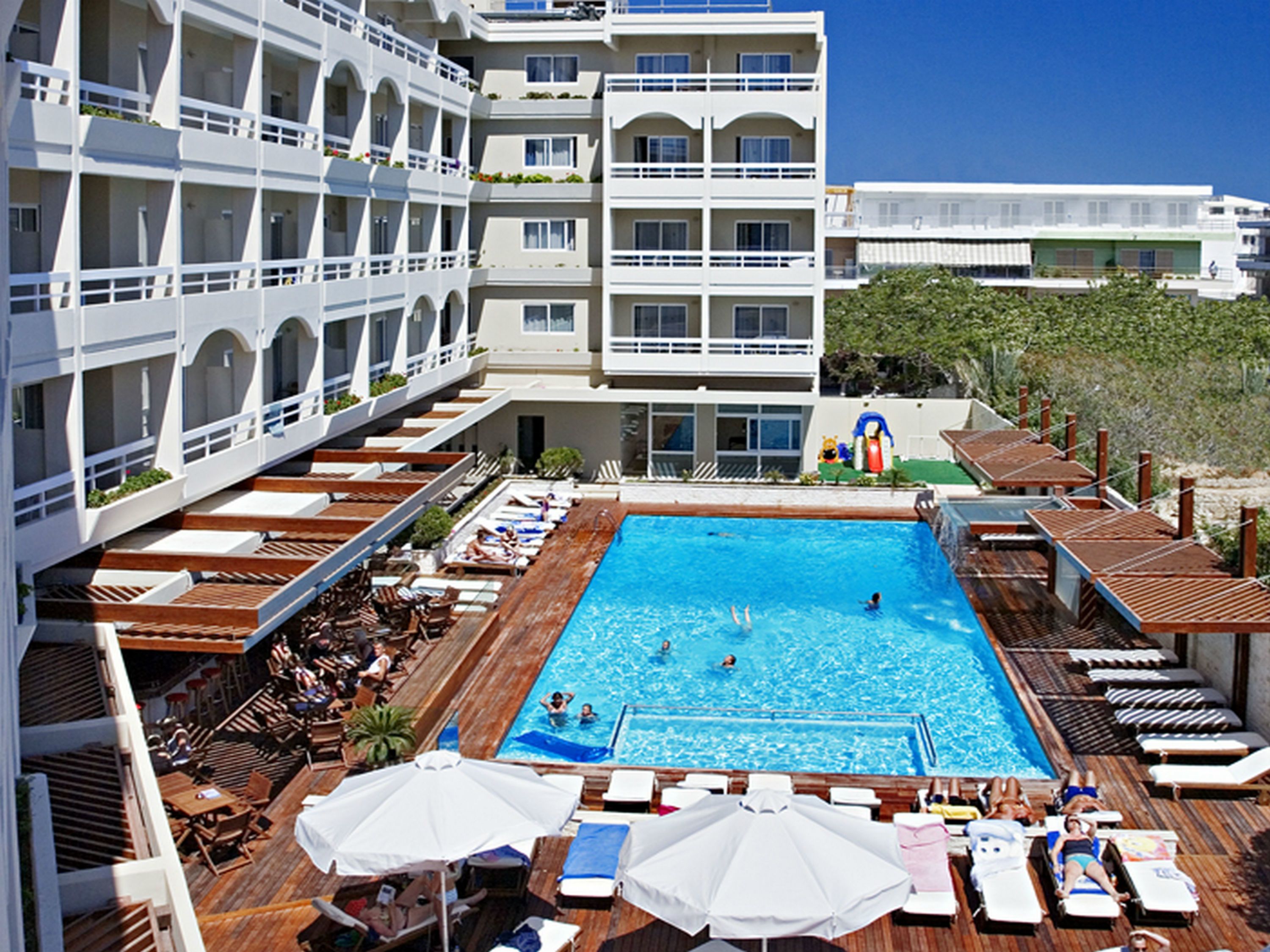 Un hôtel doté d’une grande piscine, de nombreux balcons et d’un espace extérieur aménagé pour s’asseoir.