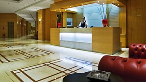 A hotel reception area with a modern design, featuring a reception desk, a red leather sofa, and a patterned floor. - Athineon Hotel (Rhodes)