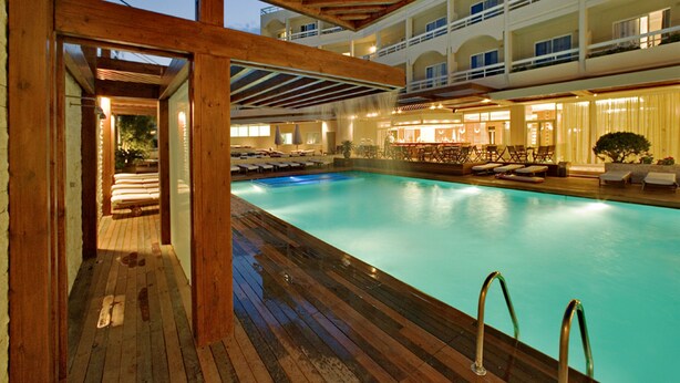 A swimming pool with wooden deck and lounge chairs, surrounded by a multi-level building with balconies. - Athineon Hotel (Rhodes)