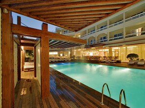 A swimming pool with wooden deck and lounge chairs, surrounded by a multi-level building with balconies. - Athineon Hotel (Rhodes)