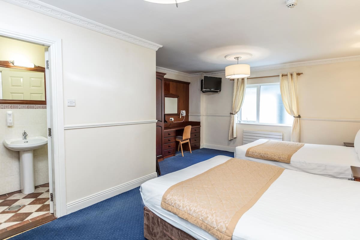 A hotel room with two beds, a desk, a chair, a television, and a bathroom with a sink and mirror.