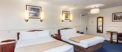 A hotel room with two single beds, a wooden headboard, a small table, a chair, and a mirror.
