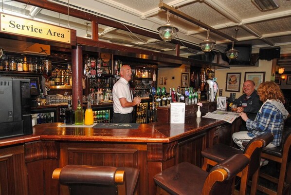 Una zona de bar con un letrero de servicio, un bartender y clientes.