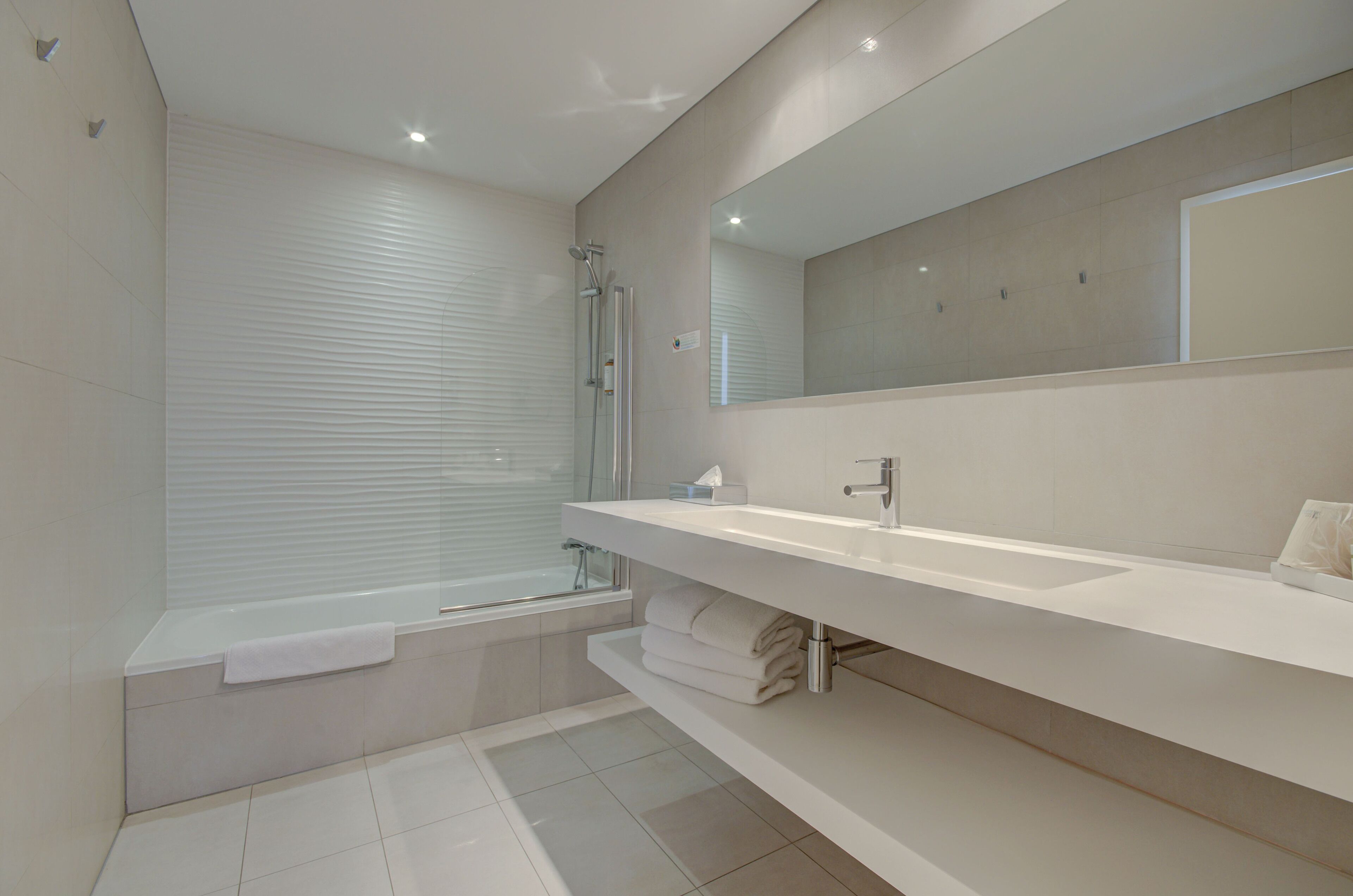 A modern bathroom with a bathtub, a large mirror, and a white vanity.