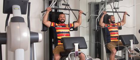 A man exercising on a gym machine with a mirror and a treadmill in the background.