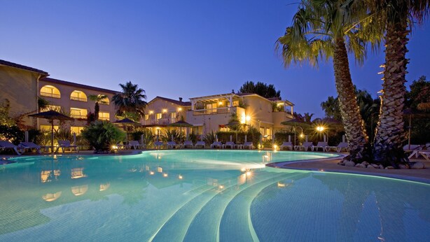 Un hotel con una piscina grande, palmeras y varios edificios con balcones.