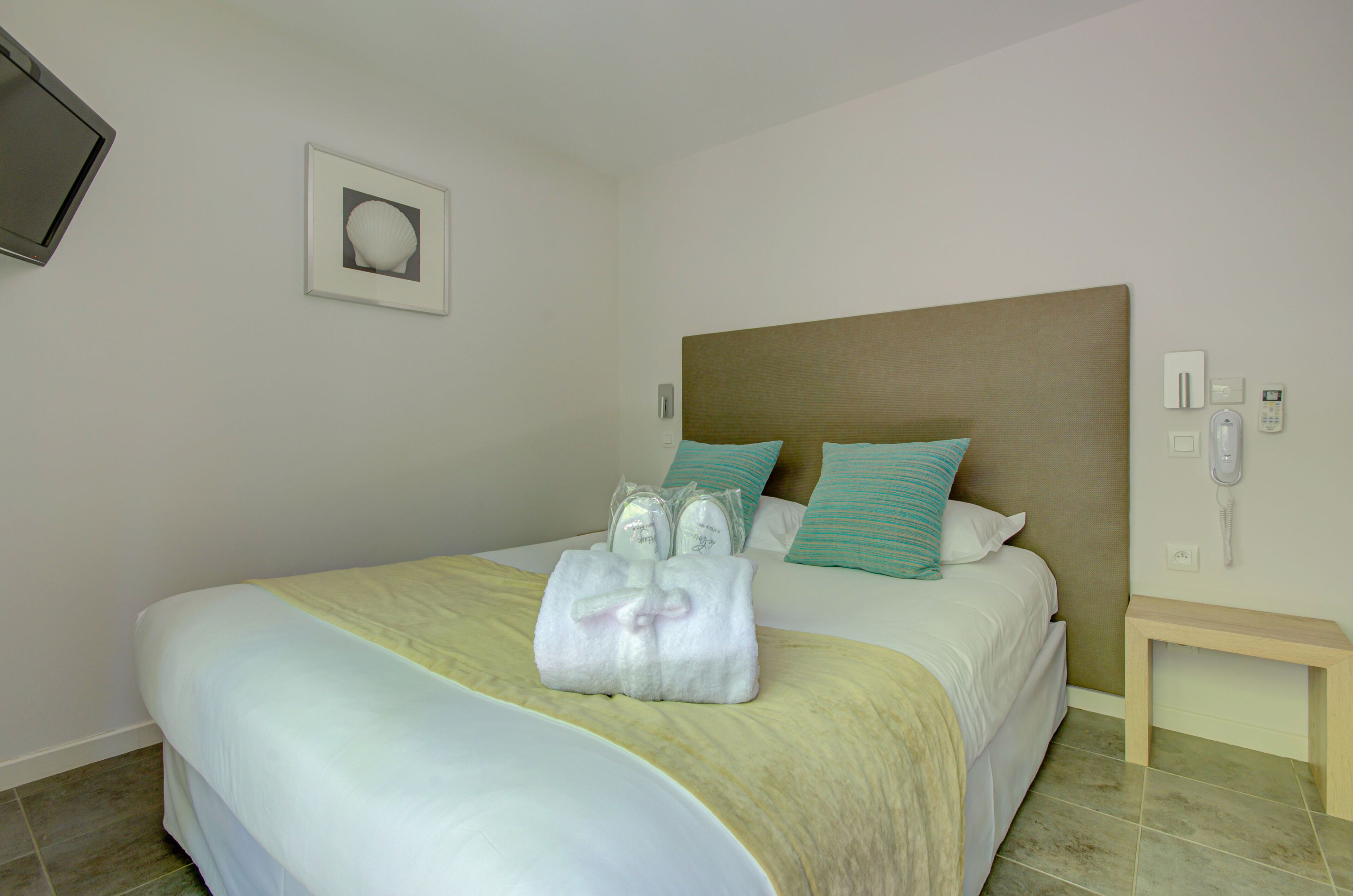 A neatly made bed with a headboard, a bedside table with a phone, and a picture on the wall.