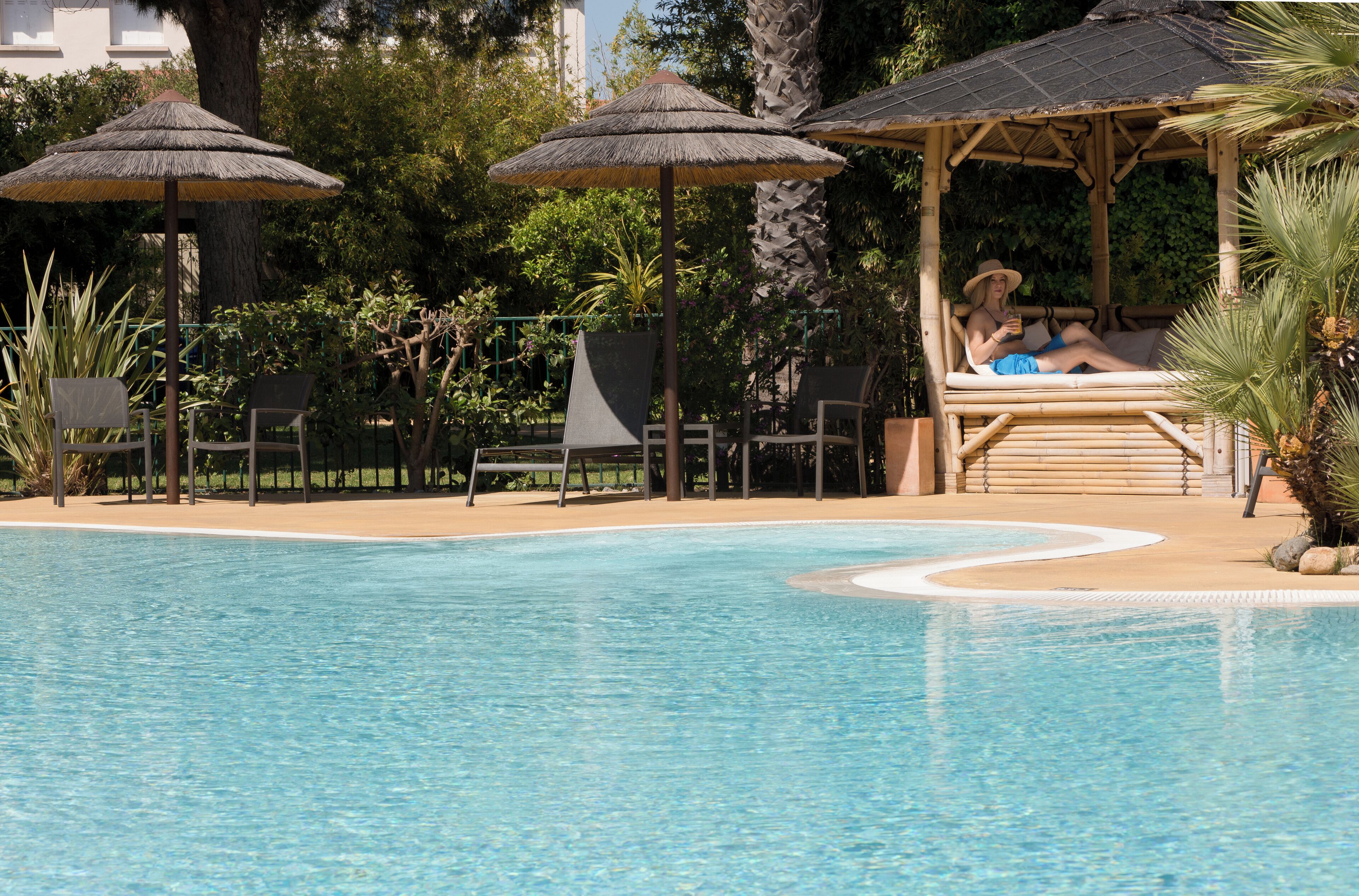 A swimming pool with lounge chairs and umbrellas, surrounded by greenery and a wooden gazebo.