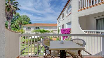 Un balcon avec une table et des chaises, donnant sur un jardin et un bâtiment doté de fenêtres en arc de cercle.