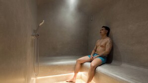 Una persona sentada en un entorno tipo spa, con una ducha y piso de azulejos.
