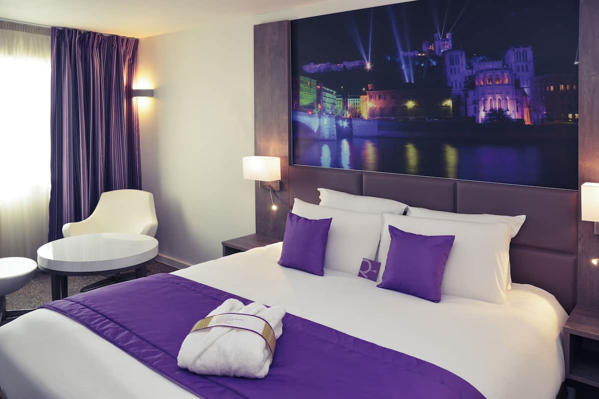 A hotel room with a large bed, two pillows, a bedside table, a chair, and a nightstand.