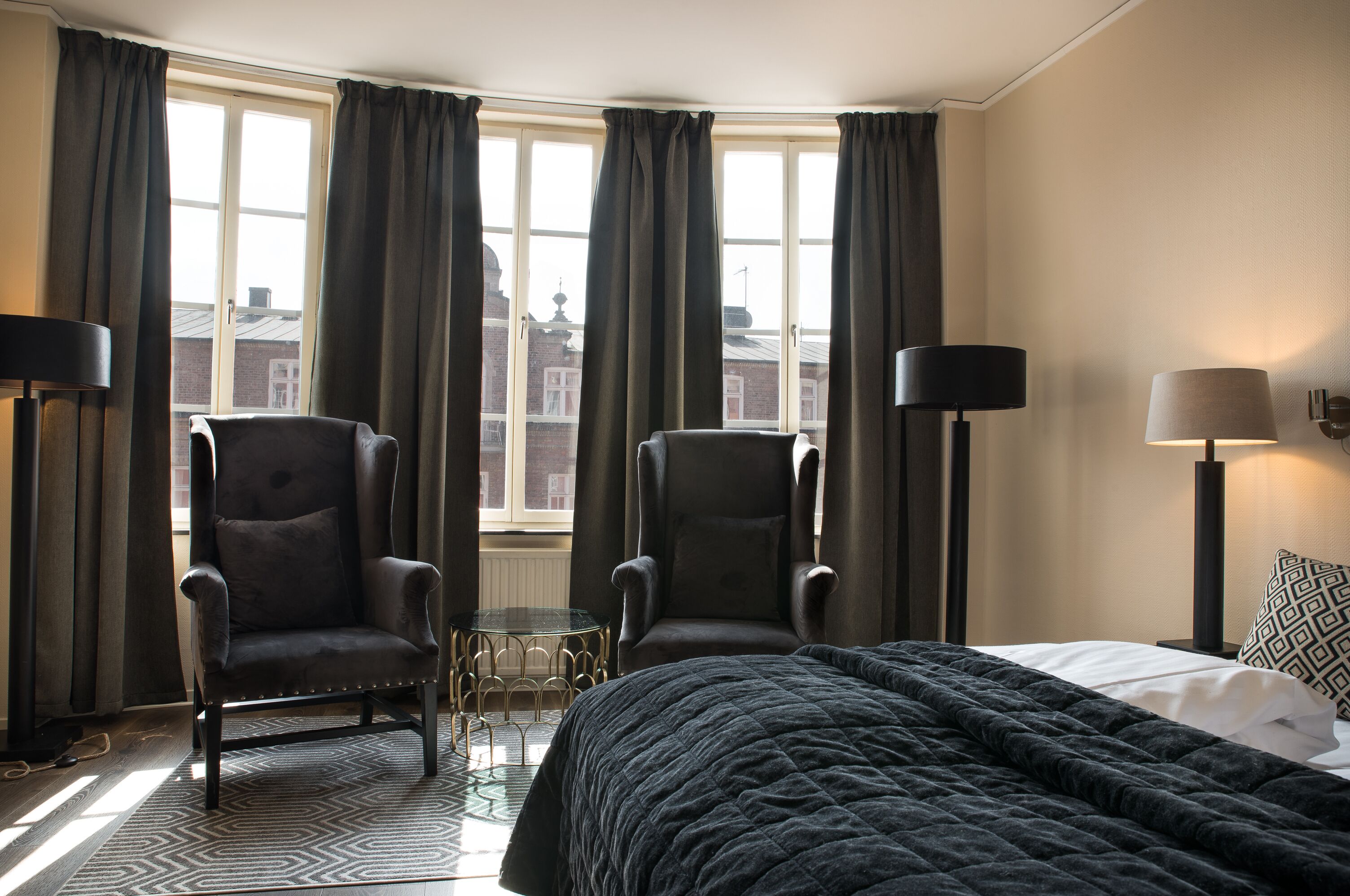 Une chambre d’hôtel avec un grand lit, deux fauteuils, une petite table et deux lampes.