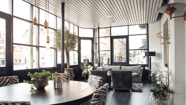A modern interior with a round table, zebra-patterned chairs, a sofa, and large windows offering a city view.