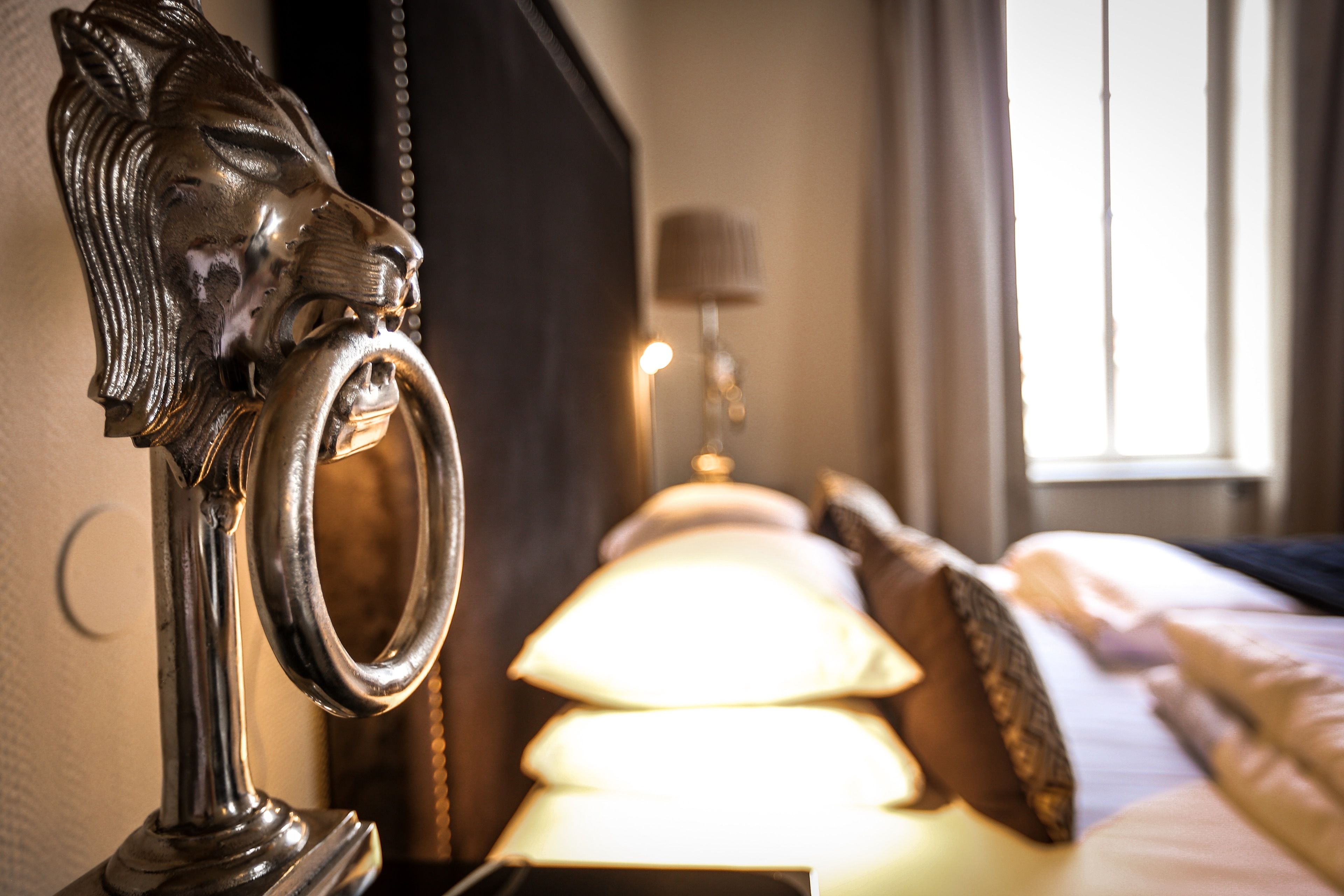 Een bed met hoofdbord, een lamp en een raam met gordijnen.