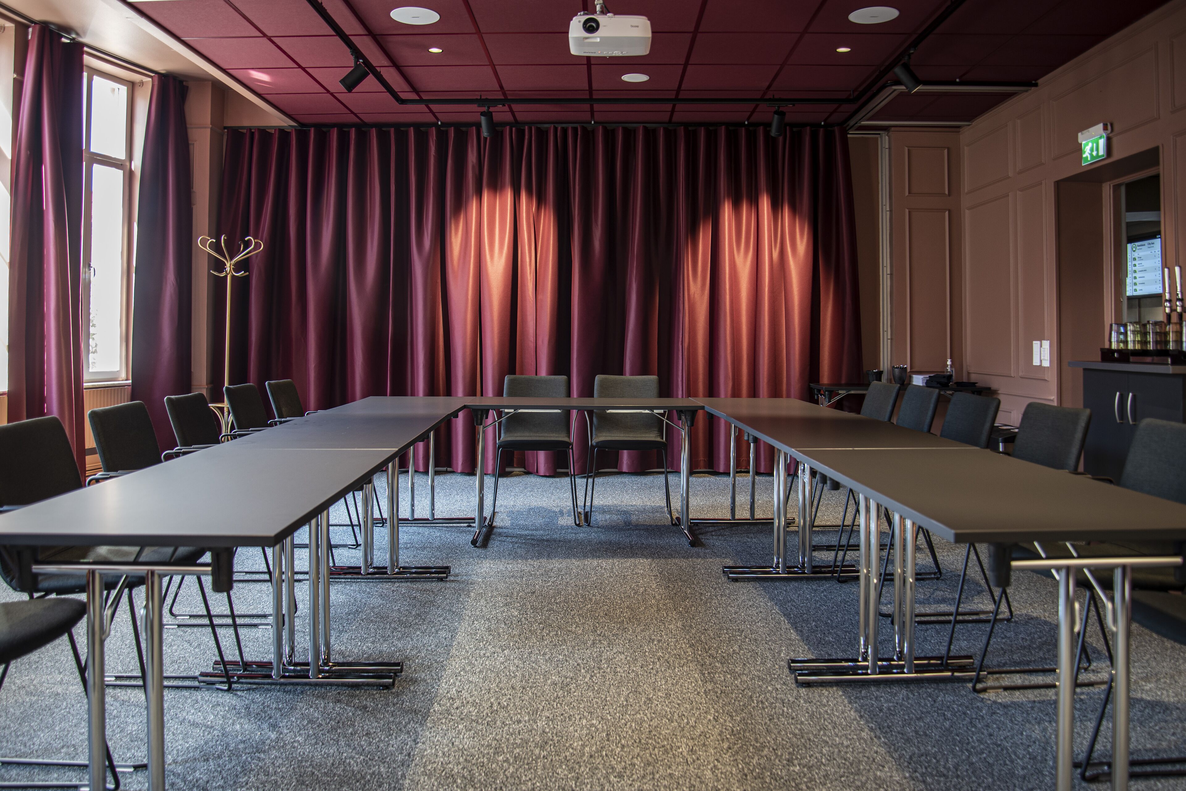 A conference room with a long table, chairs, a projector, and curtains.