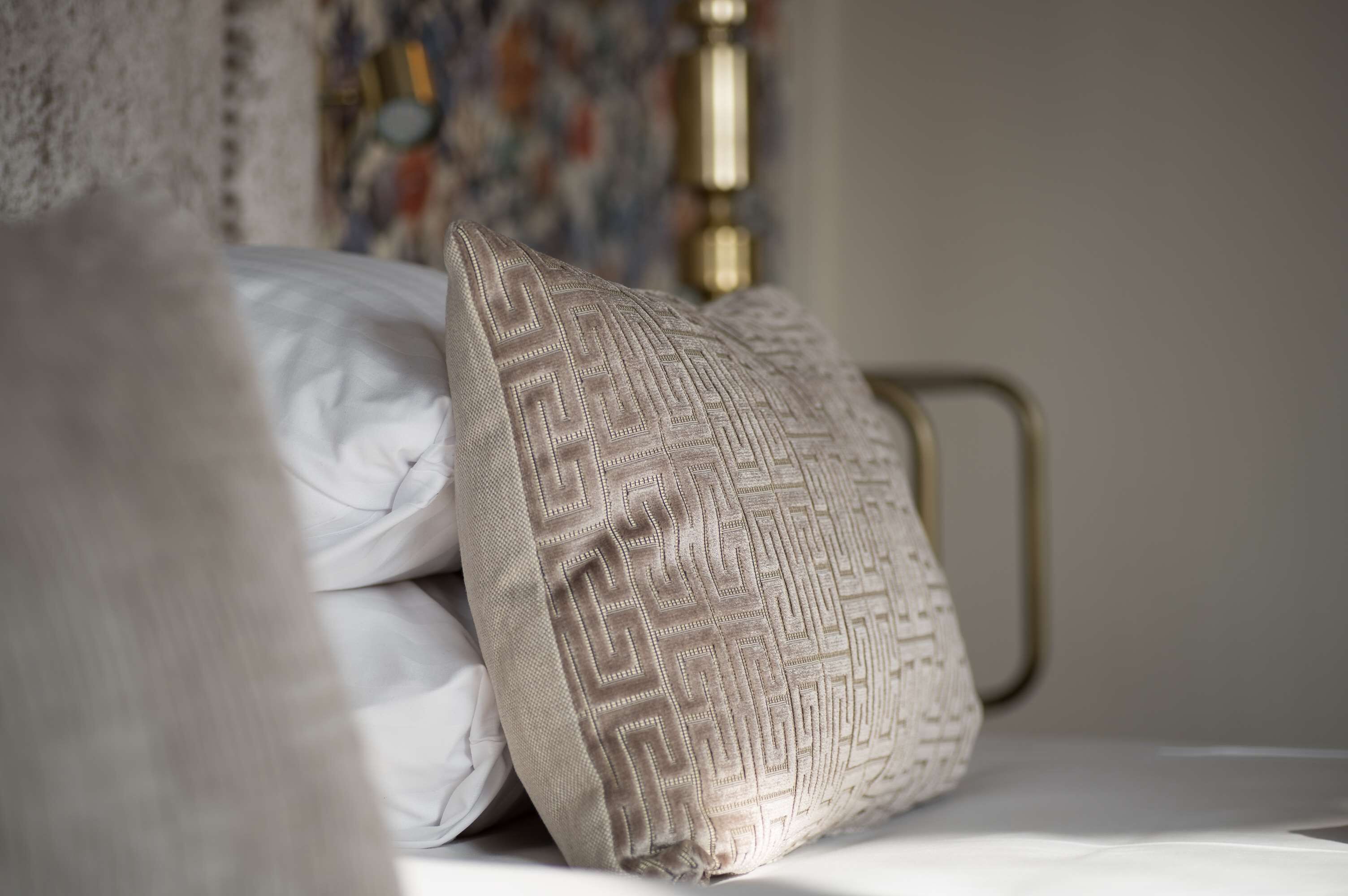 Un letto con biancheria bianca e un cuscino decorativo con motivo geometrico.