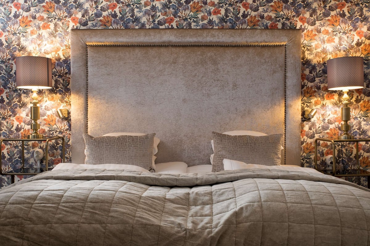 Une chambre à coucher avec un grand lit, un papier peint à motifs floraux et deux lampes de chevet.