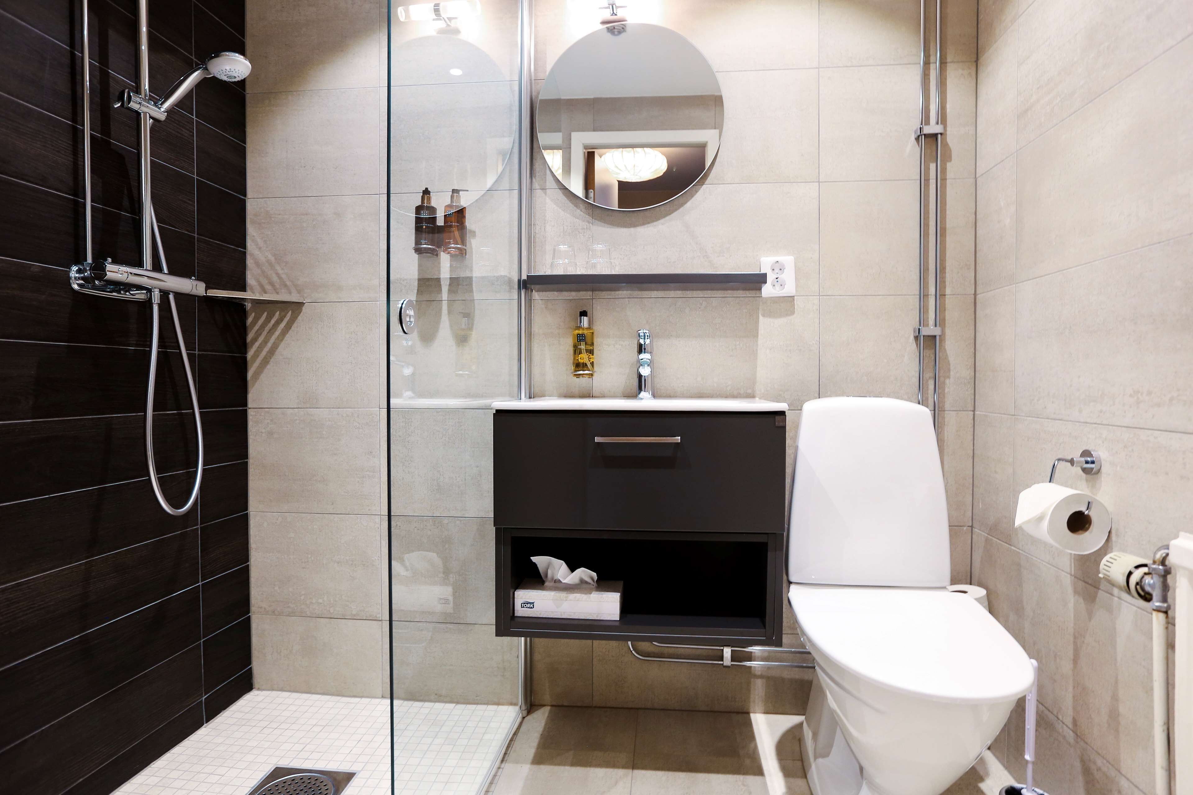 Une salle de bain moderne avec une douche à parois de verre, des toilettes, un lavabo avec un miroir et une étagère contenant des articles de toilette.