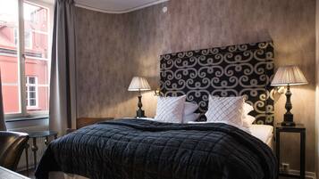 A hotel room with a large bed, two bedside lamps, a headboard with a patterned design, and a view of a building outside.