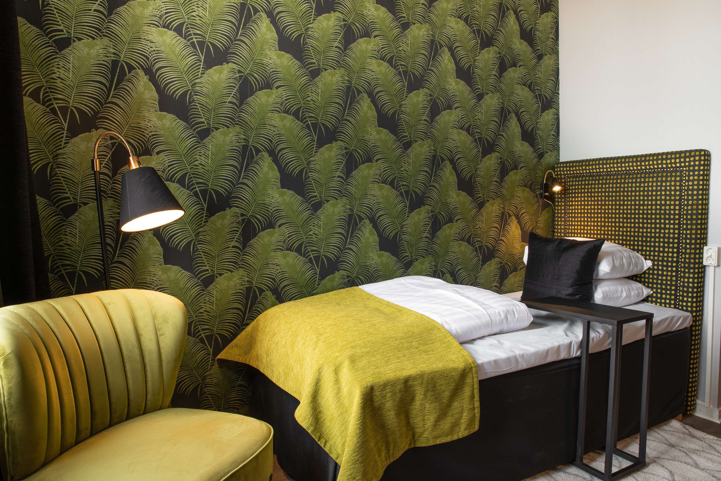 A room with a bed, a chair, a lamp, and a wall with a leaf pattern.