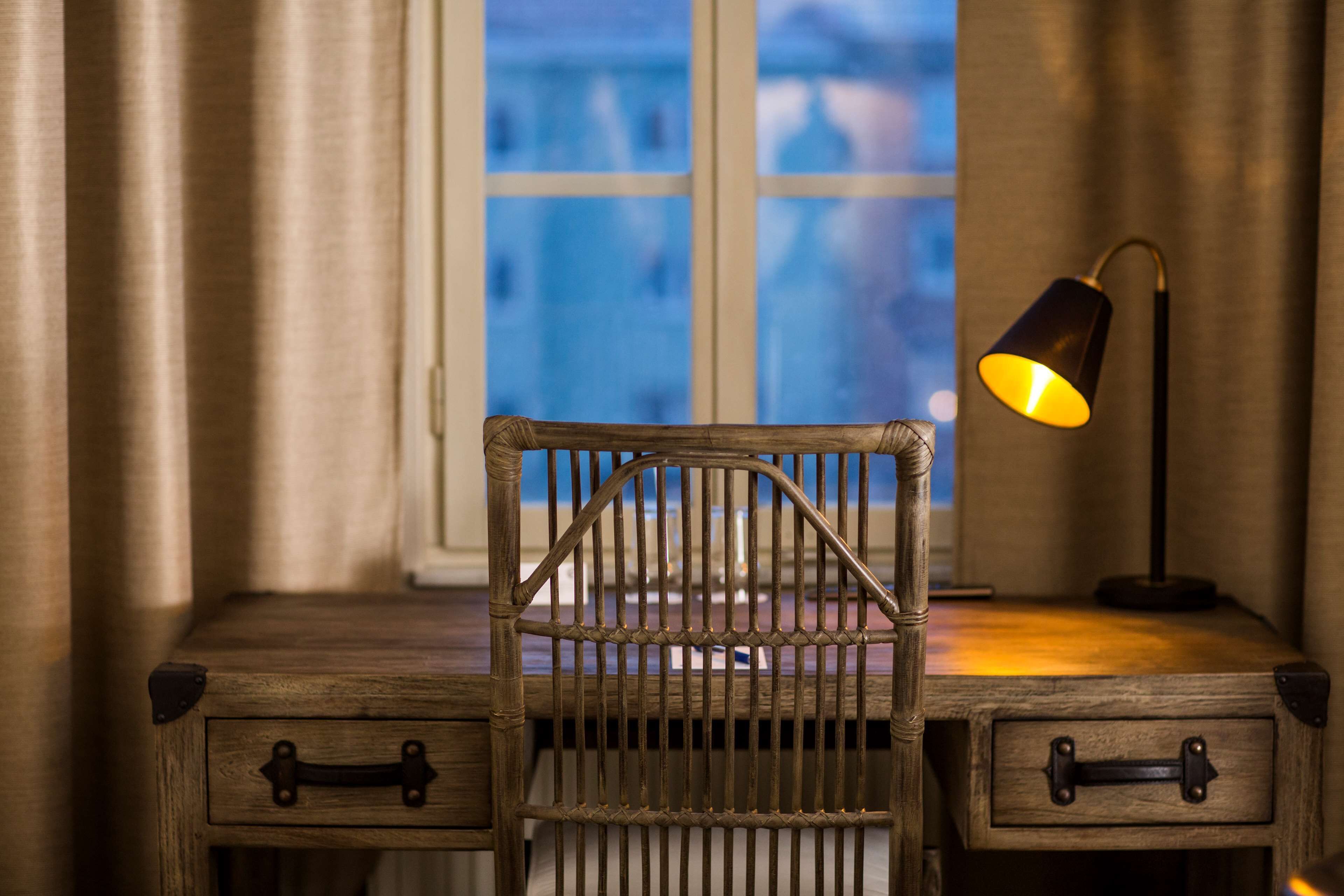 Een houten bureau met een rieten stoel en een lamp.