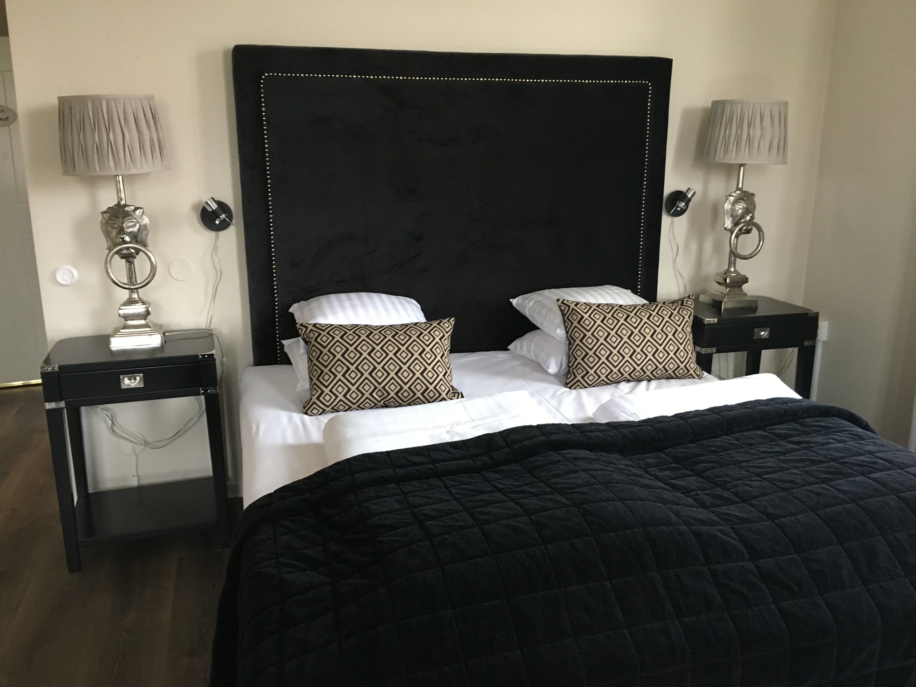 Una habitación de hotel con una cama grande, dos mesitas de noche con lámparas y un cabecero oscuro.