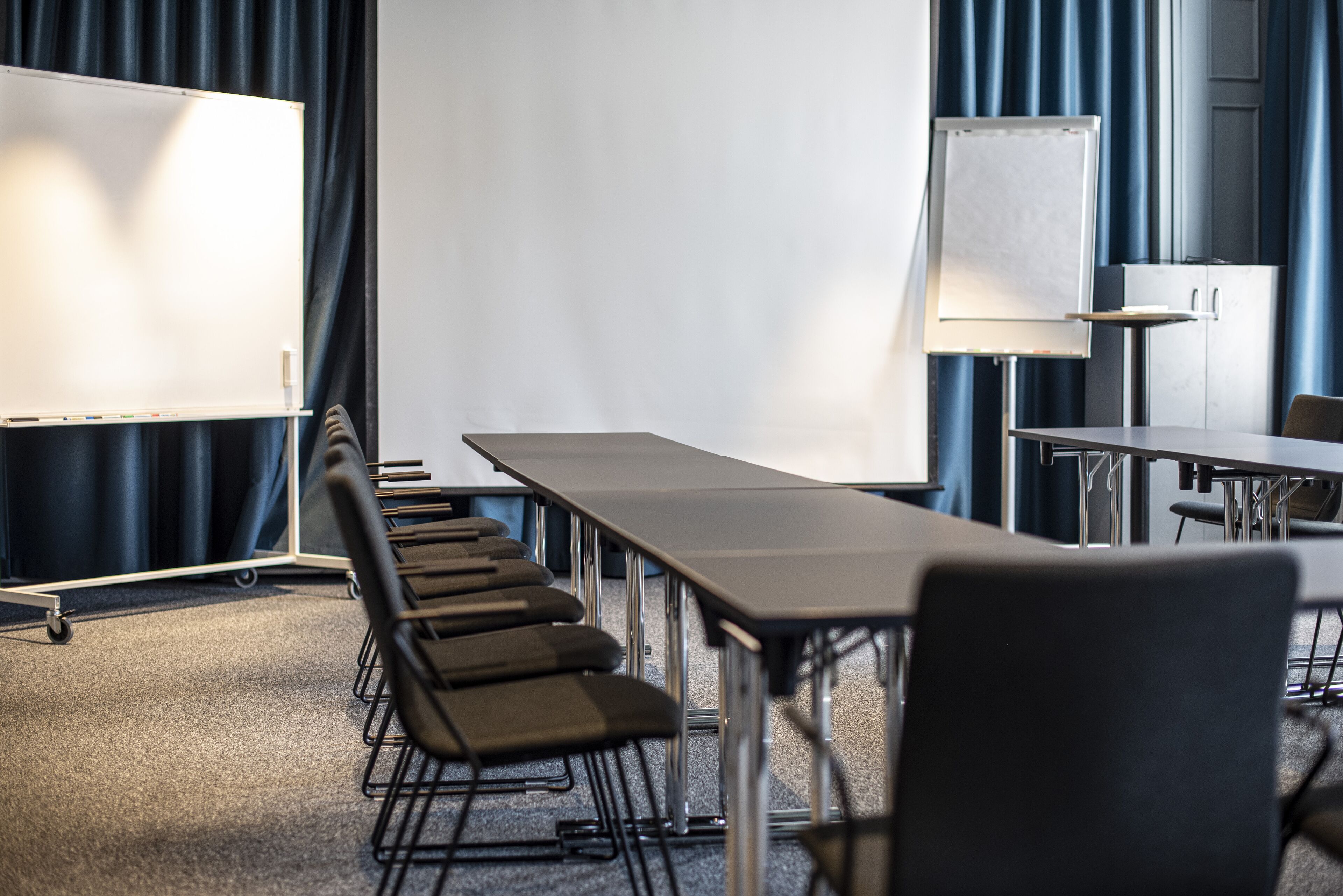 A conference room with a long table, chairs, a whiteboard, and a projector screen.