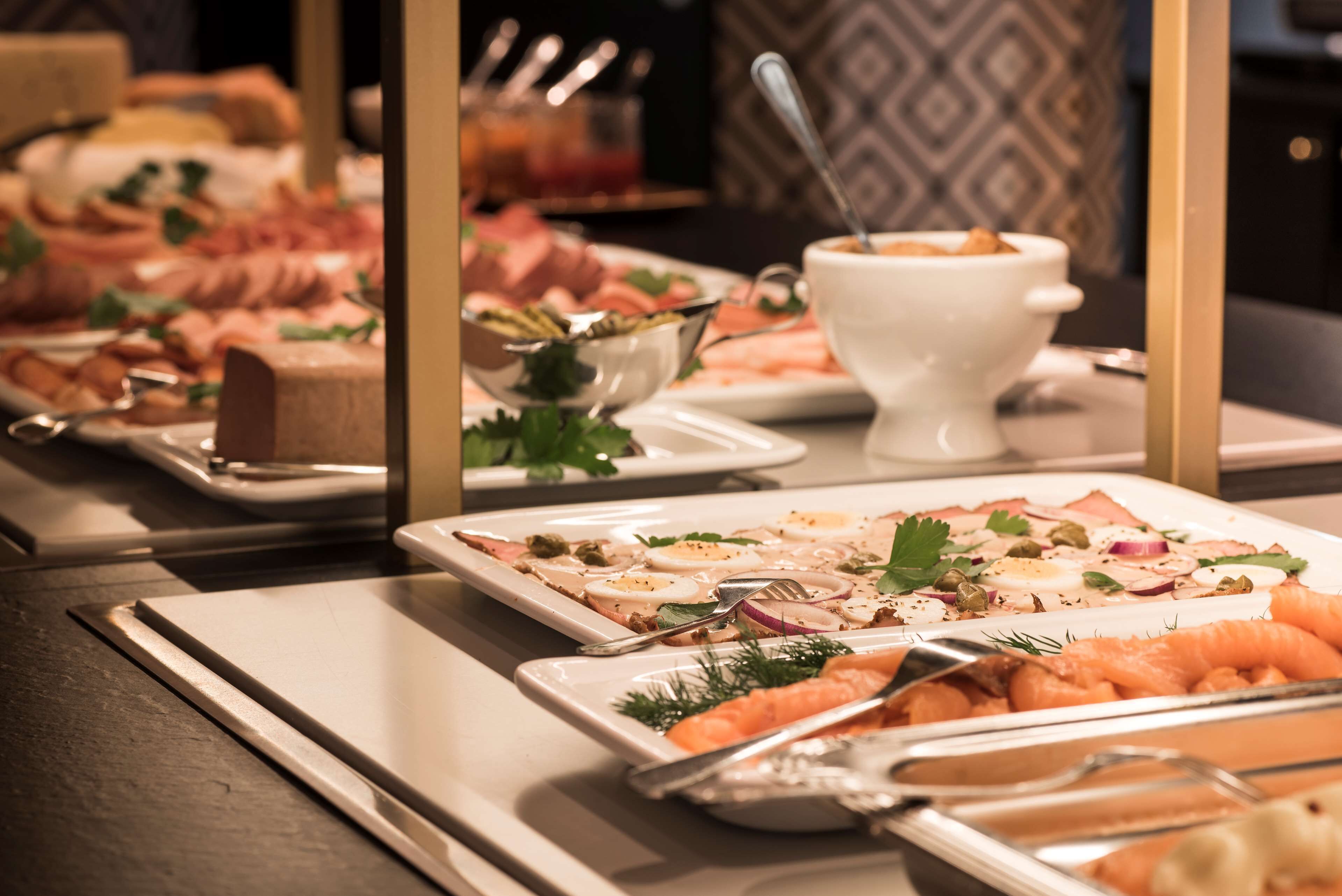 Mesa de buffet com diversos pratos, incluindo salmão, legumes e uma tigela branca com uma colher.