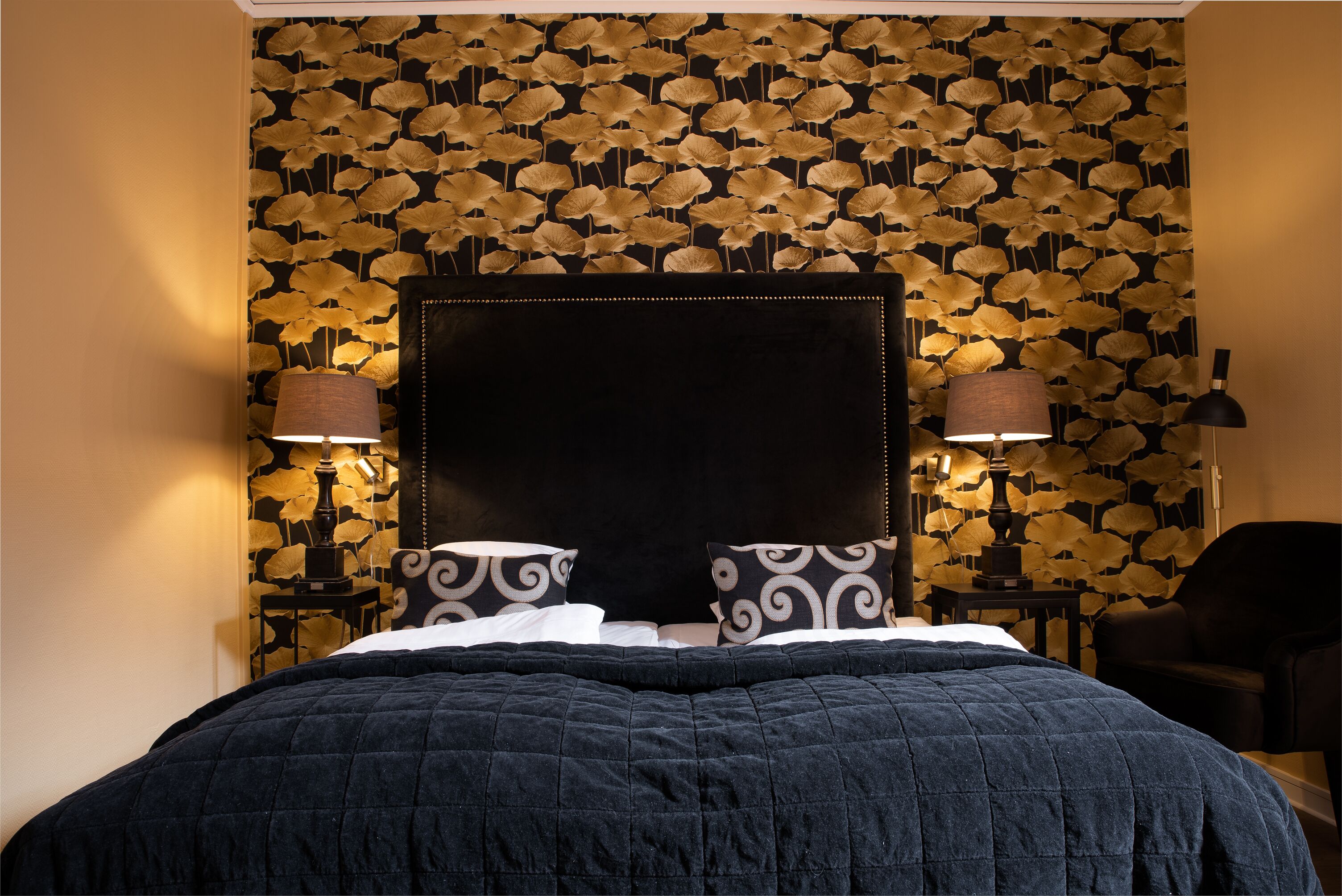 A bed with a black headboard, two bedside lamps, and patterned pillows.
