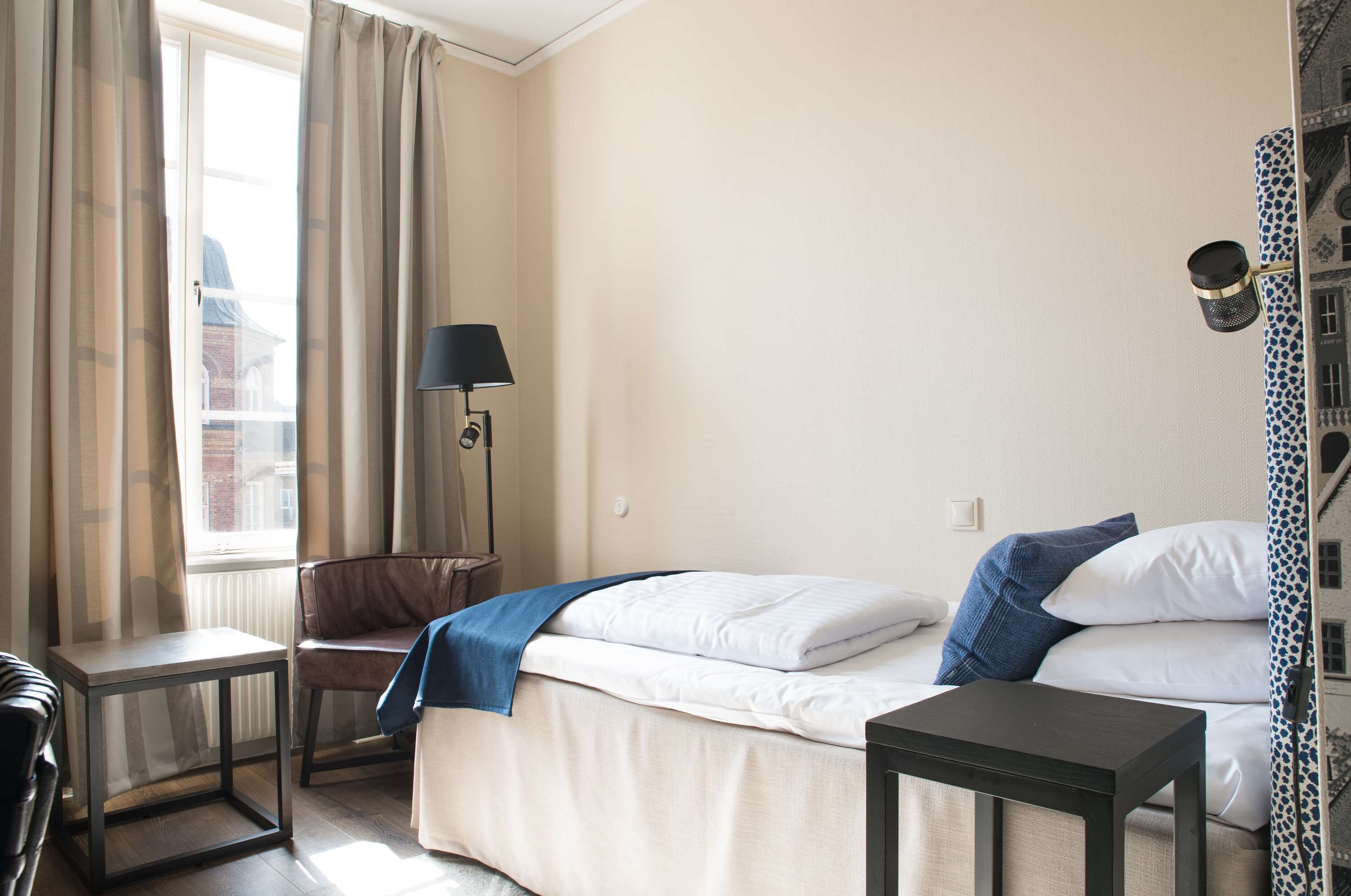 Habitación de hotel con cama, escritorio, silla, lámpara y vista a la ciudad a través de la ventana.