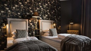 A hotel room with two beds, a nightstand, a lamp, and a floral wallpaper.